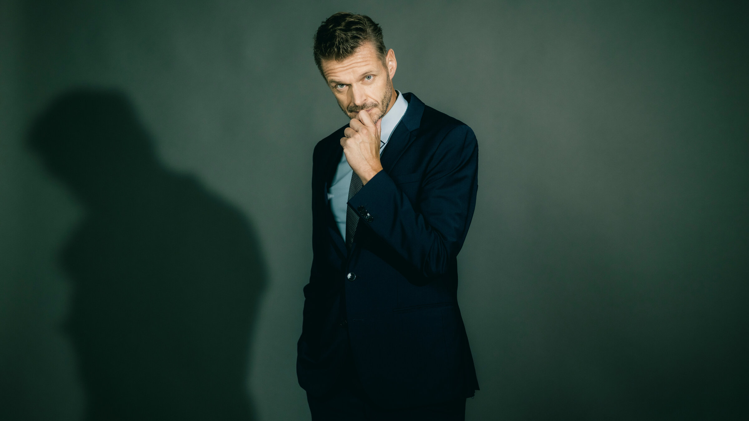 "JOURNAL DELUXE": Florian Schroeder steht in der Mitte des Bildes. Er hÃ¤lt sich die linke Hand an sein Kinn. Er trÃ¤gt einen dunklen Anzug.