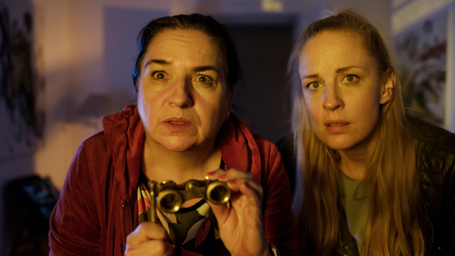 "SOKO Wien - Aussicht mit Mord": Gerichtsmedizinerin Dr. Franziska Beck (Maria Happel) steht zusammen mit Gruppeninspektorin Penny Lanz (Lilian Klebow) am Fenster. Sie schauen gebannt zur Nachbarin. Dr. Beck hält ein kleines Opernglas in den Händen.