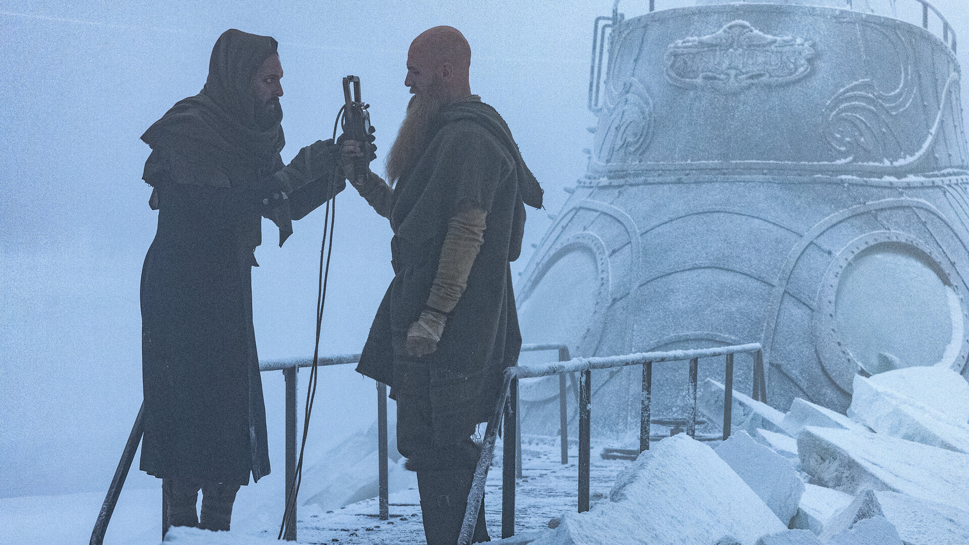 "Nautilus - Gefangen im Eis": Nemo (Shazad Latif) und Jiacomo (Andrew Shaw) stehen sich auf dem vereisten U-Boot Nautilus gegenüber. Nemo übergibt Jiacomo einen Gegenstand, an dem ein langes Kabel befestigt ist.