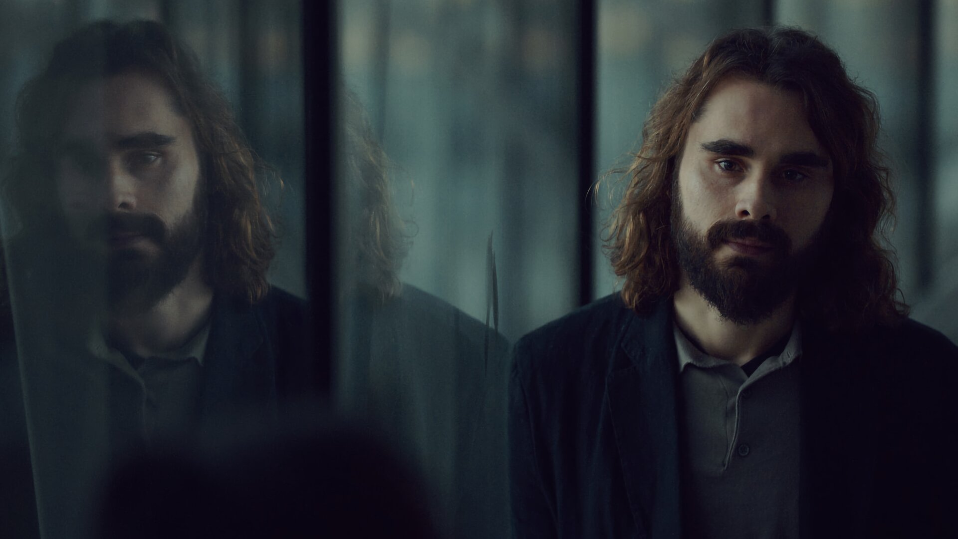 "Moresnet - The Book of Death: Der Preis der Erinnerung": Ben Schotz (Boris Van Severen) steht neben einer großen Spiegelfläche und schaut gedankenverloren nach vorne. Links von ihm ist sein Spiegelbild zu erkennen.