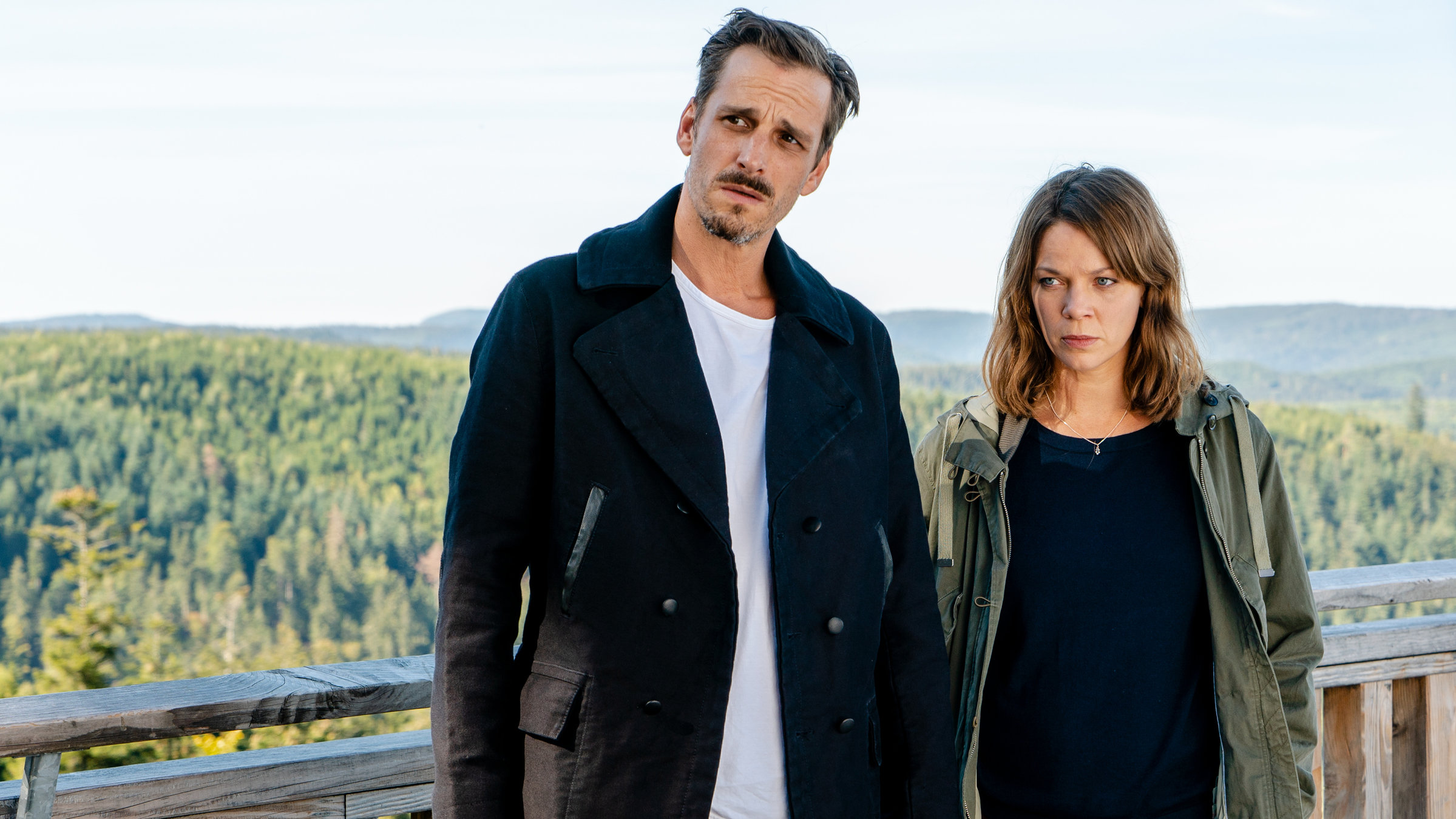 "Und tot bist Du! (2)": Konrad Diener (Max von Thun) und Maris Bächle (Jessica Schwarz) stehen auf einer Plattform. Im Hintergrund Wald und Hügel.