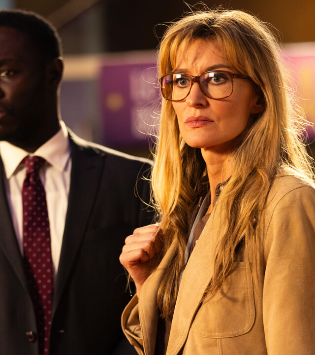 "The Kollective - Eine heiße Spur": Maya (Natascha McElhone) und Senator Lusamba (Ralph Amoussou) stehen nebeneinander in einem Gebäude. Sie beobachten etwas.