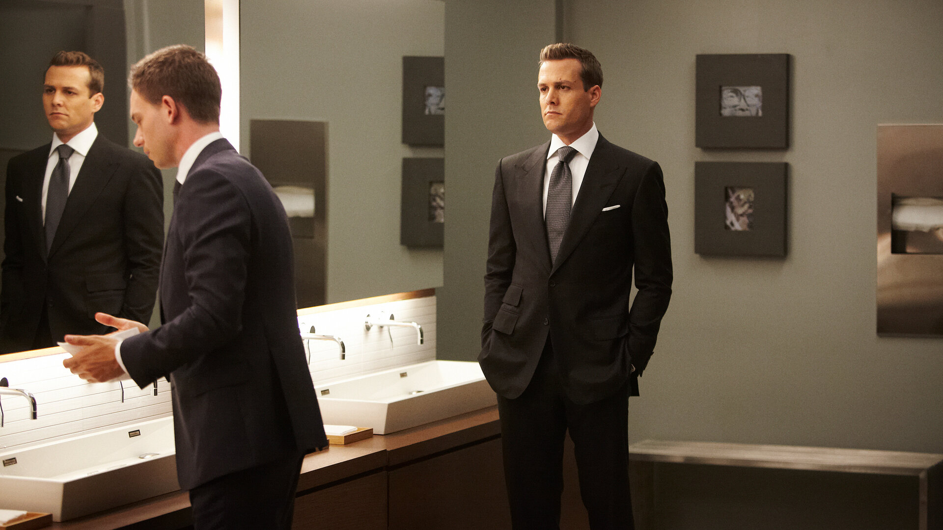 "Suits - Herzenssache": In einem Toilettenraum: Mike (Patrick J. Adams) steht an einem Waschtisch vor einem großen Spiegel, während Harvey (Gabriel Macht) mit ernster Miene im Raum steht und ihn beobachtet.