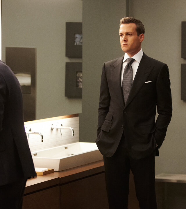 "Suits - Herzenssache": In einem Toilettenraum: Mike (Patrick J. Adams) steht an einem Waschtisch vor einem großen Spiegel, während Harvey (Gabriel Macht) mit ernster Miene im Raum steht und ihn beobachtet.
