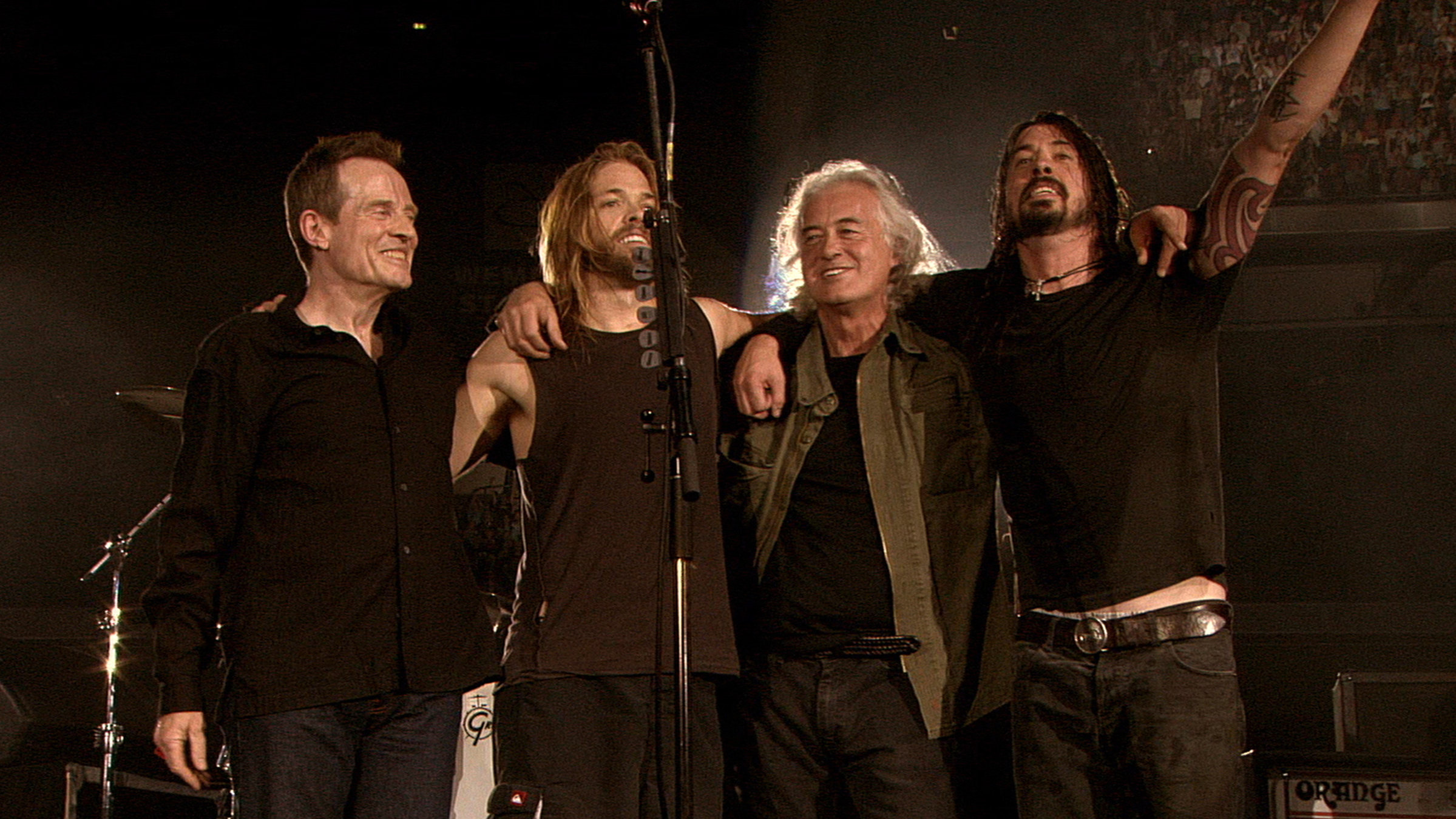 "Foo Fighters: Live at Wembley Stadium": Die Mitglieder der Band Foo Fighters stehen nebeneinander auf einer Bühne, die Arme um die Schultern des Nebenmannes gelegt.