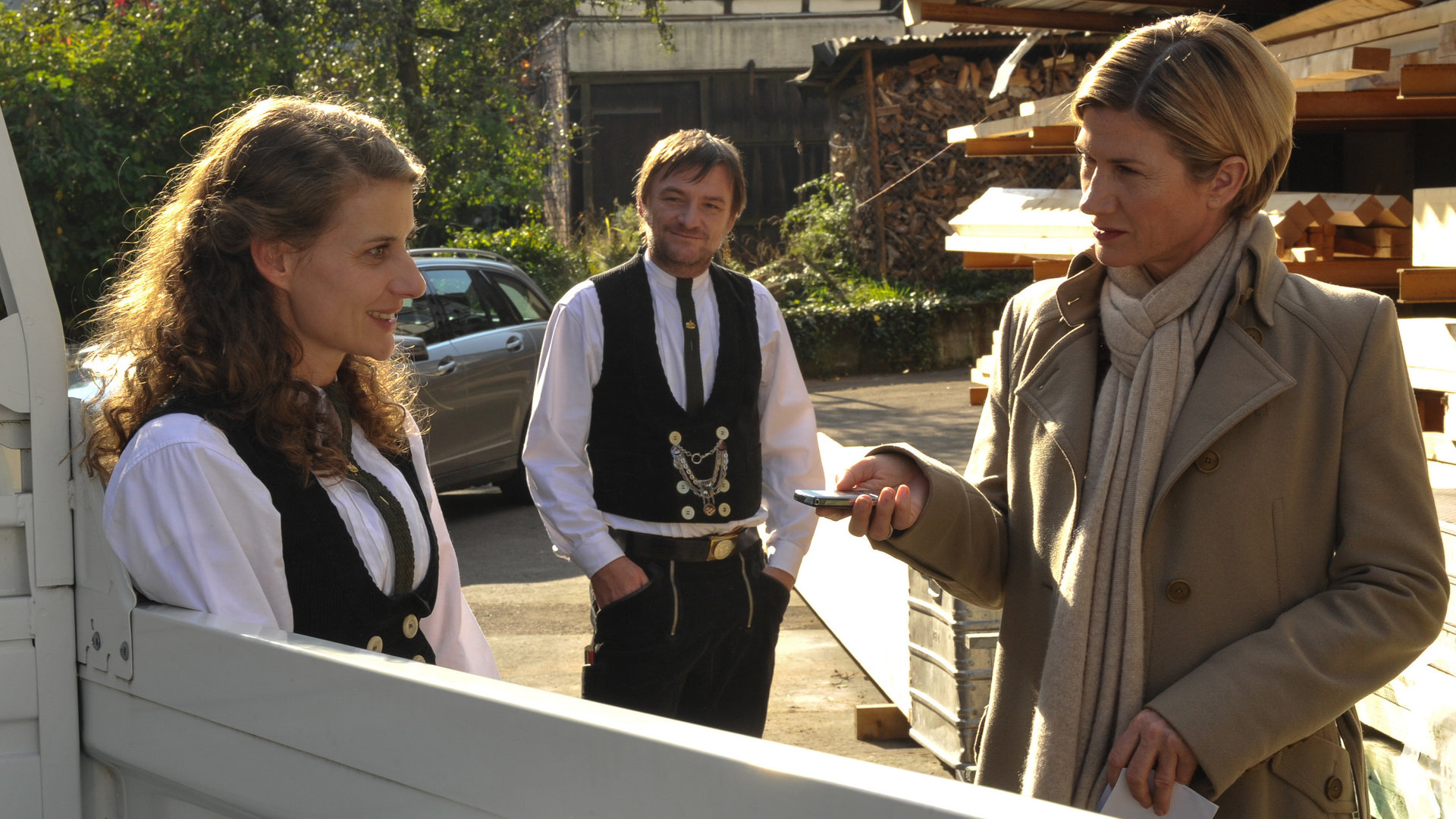 "SOKO Stuttgart - Schlitzohr": Die Zimmermannsfrau Karin Goldmann (Marie Rönnebeck), ihr Chef Peter Kahlert (Christian Kerepeszki) und Kommissarin Martina Seiffert (Astrid M. Fünderich) stehen redend auf dem Hof der Zimmermannswerkstatt.