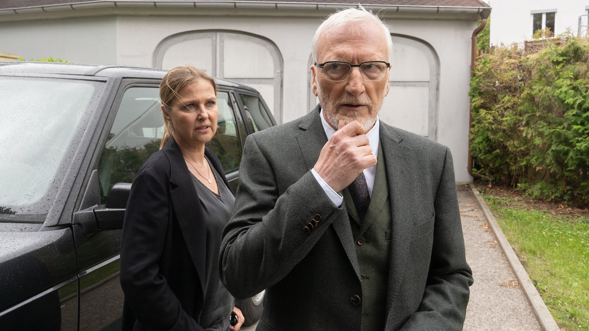 "Die Chefin - Murnau": Dr. Jakob Murnau (Ernst Stötzner) steht nachdenklich in der Auffahrt vor seinem schwarzen SUV. Hinter ihm steht Vera Lanz (Katharina Böhm), die ihn kritisch betrachtet.