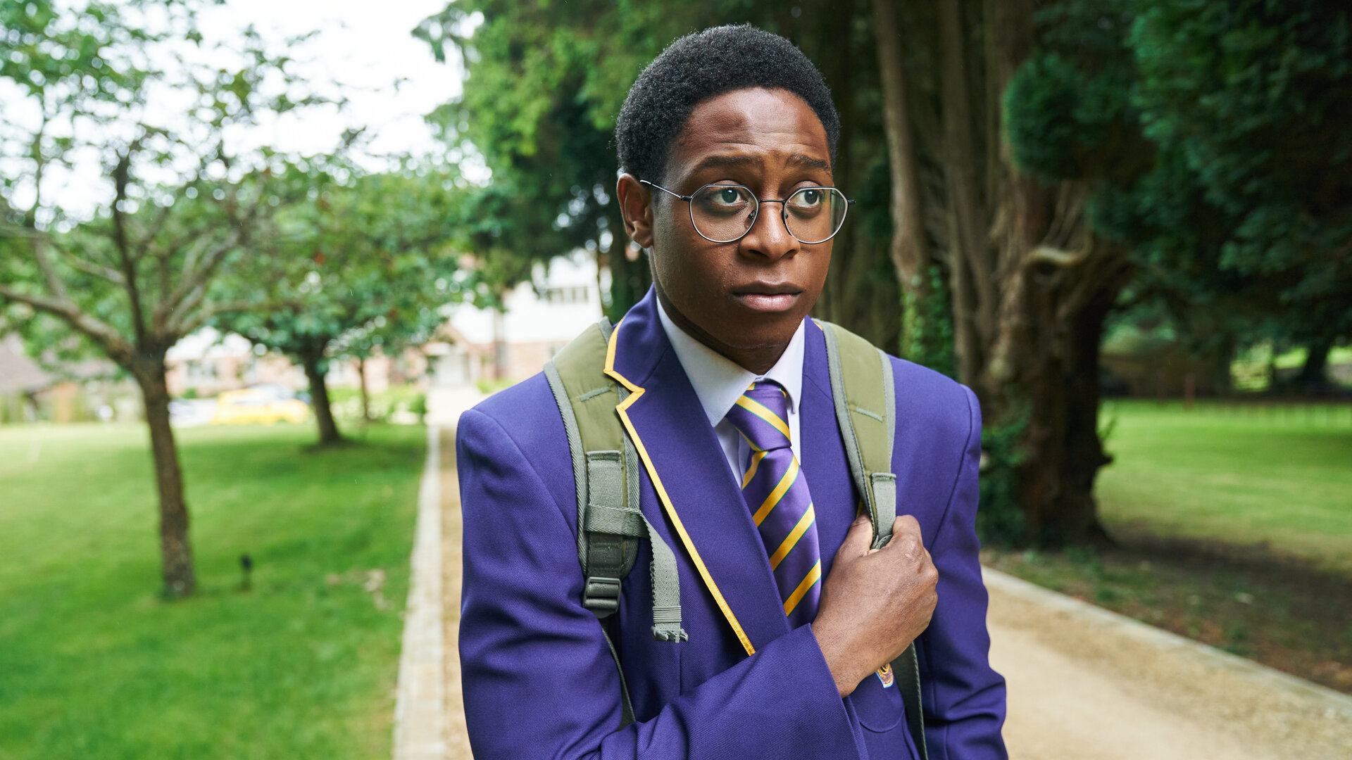 "Boarders - Welcome to St. Gilbert's - Jobs & Jealousy": Omar (Myles Kamwendo) geht auf einem Kiesweg durch den Park. Er trägt seine Schuluniform und einen Rucksack. Dabei sieht er besorgt aus.