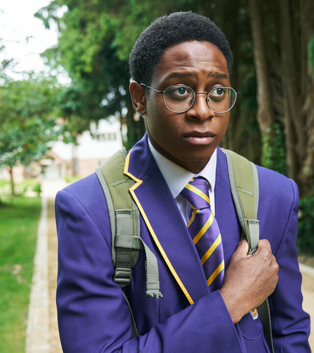 "Boarders - Welcome to St. Gilbert's - Jobs & Jealousy": Omar (Myles Kamwendo) geht auf einem Kiesweg durch den Park. Er trägt seine Schuluniform und einen Rucksack. Dabei sieht er besorgt aus.