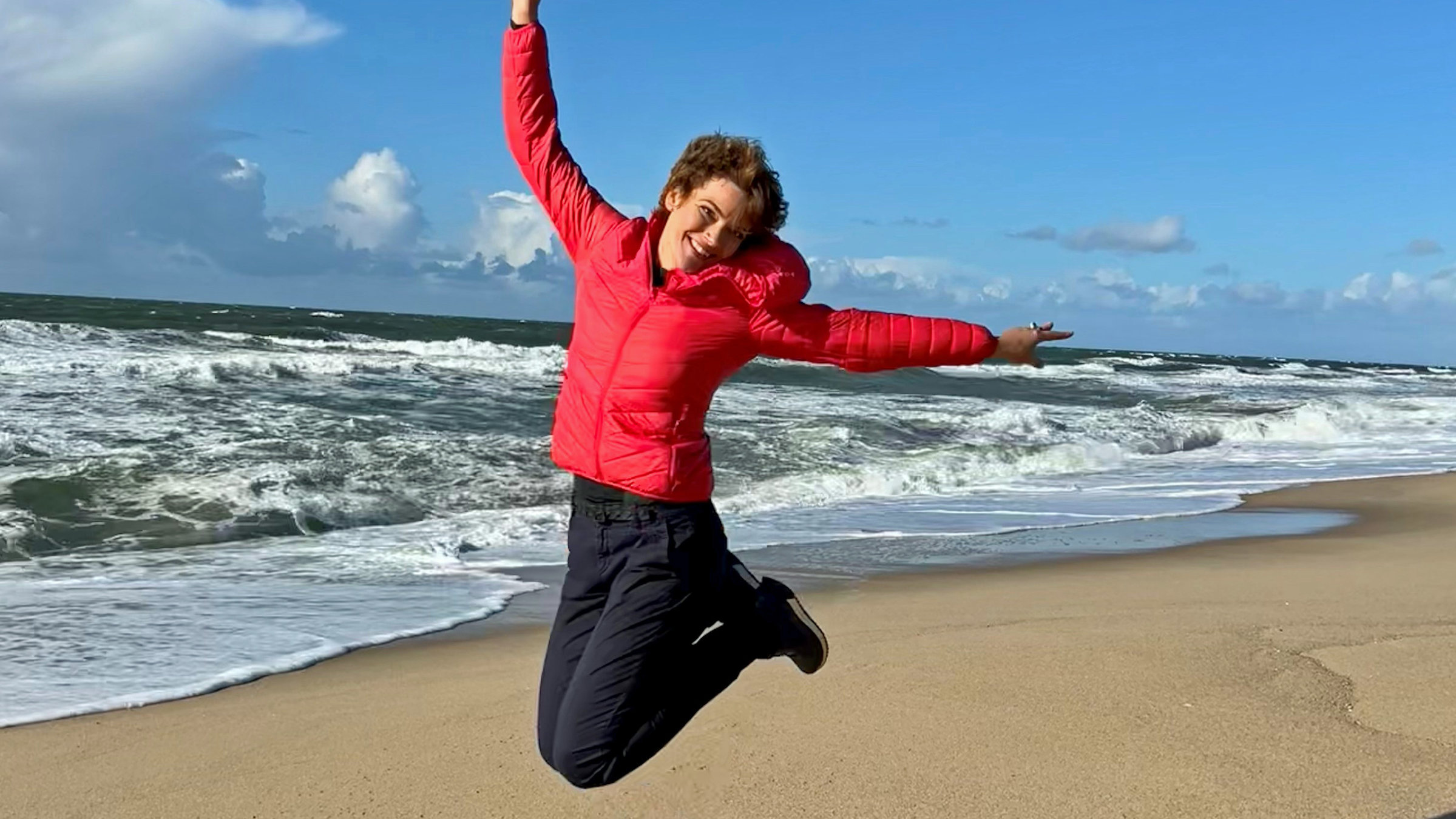 "Terra Xpress: Anders leben - der eigene Weg zum Glück": Moderatorin Lena Ganschow springt hoch und zieht die Beine nach oben. Im Hintergrund Strand und Meer.