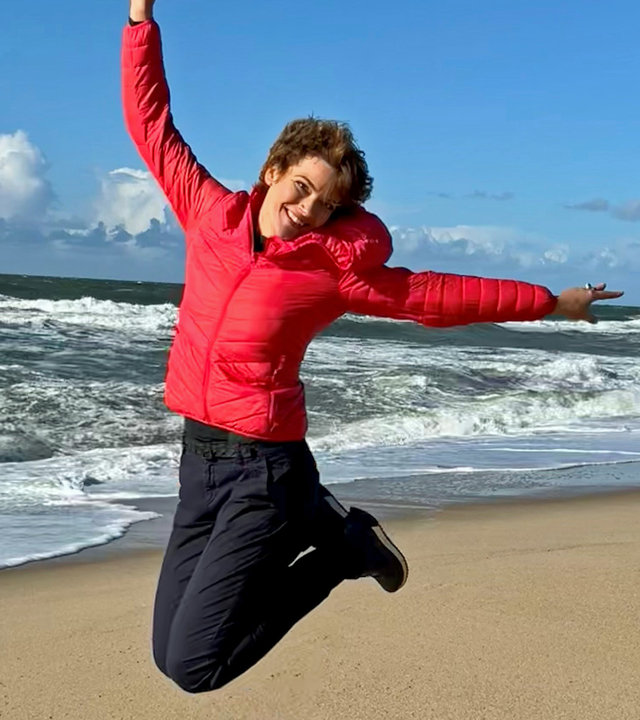 "Terra Xpress: Anders leben - der eigene Weg zum Glück": Moderatorin Lena Ganschow springt hoch und zieht die Beine nach oben. Im Hintergrund Strand und Meer.