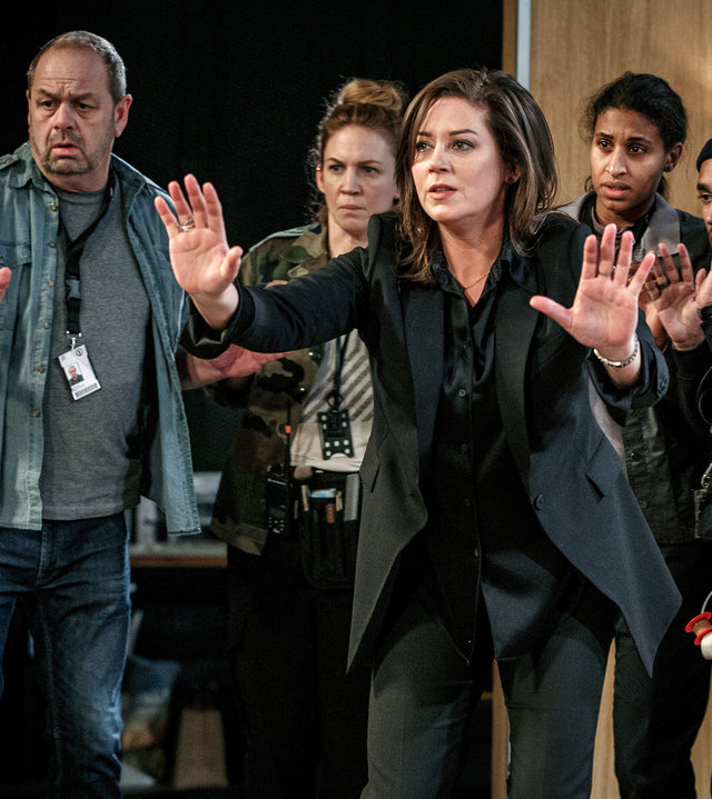 "Kommissar Beck - 58 Minuten": Alex Beijer (Jennie Silfverhjelm) steht mit erhobenen Händen in einem Fernsehstudio. Mimmi (Julia Marko-Nord) und Maya (Lola Zackow) und weitere Kollegen stehen mit angsterfülltem Blick und ebenfalls erhobenen Händen hinter Alex.