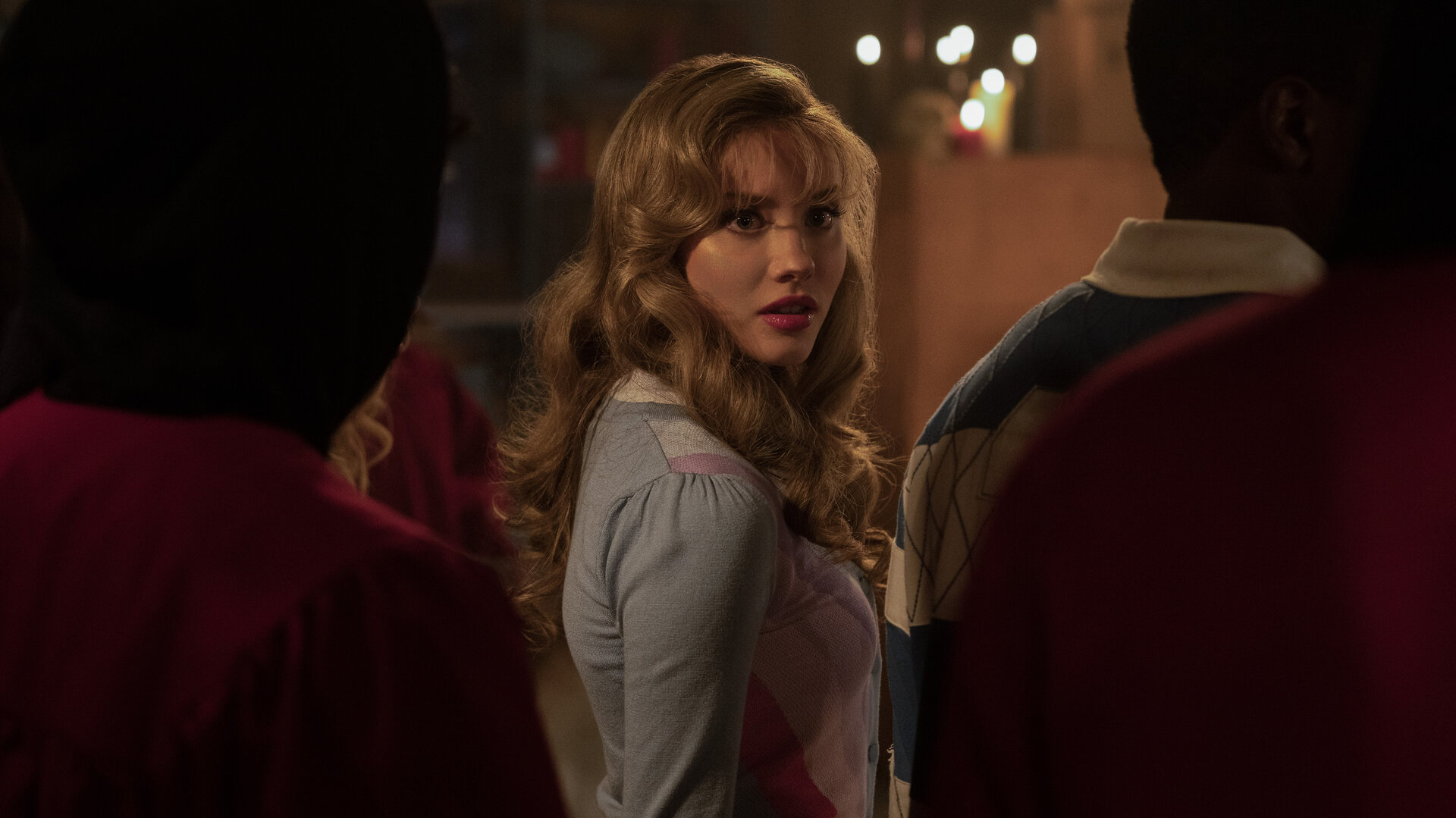 "Hysteria! - Das verlorene Herz": Judith (Jessica Treska) steht zwischen mehreren nur schemenhaft zu erkennenden Personen in einem schwach beleuchteten Raum und blickt über die Schulter zur Seite. Im Hintergrund brennen Kerzen.