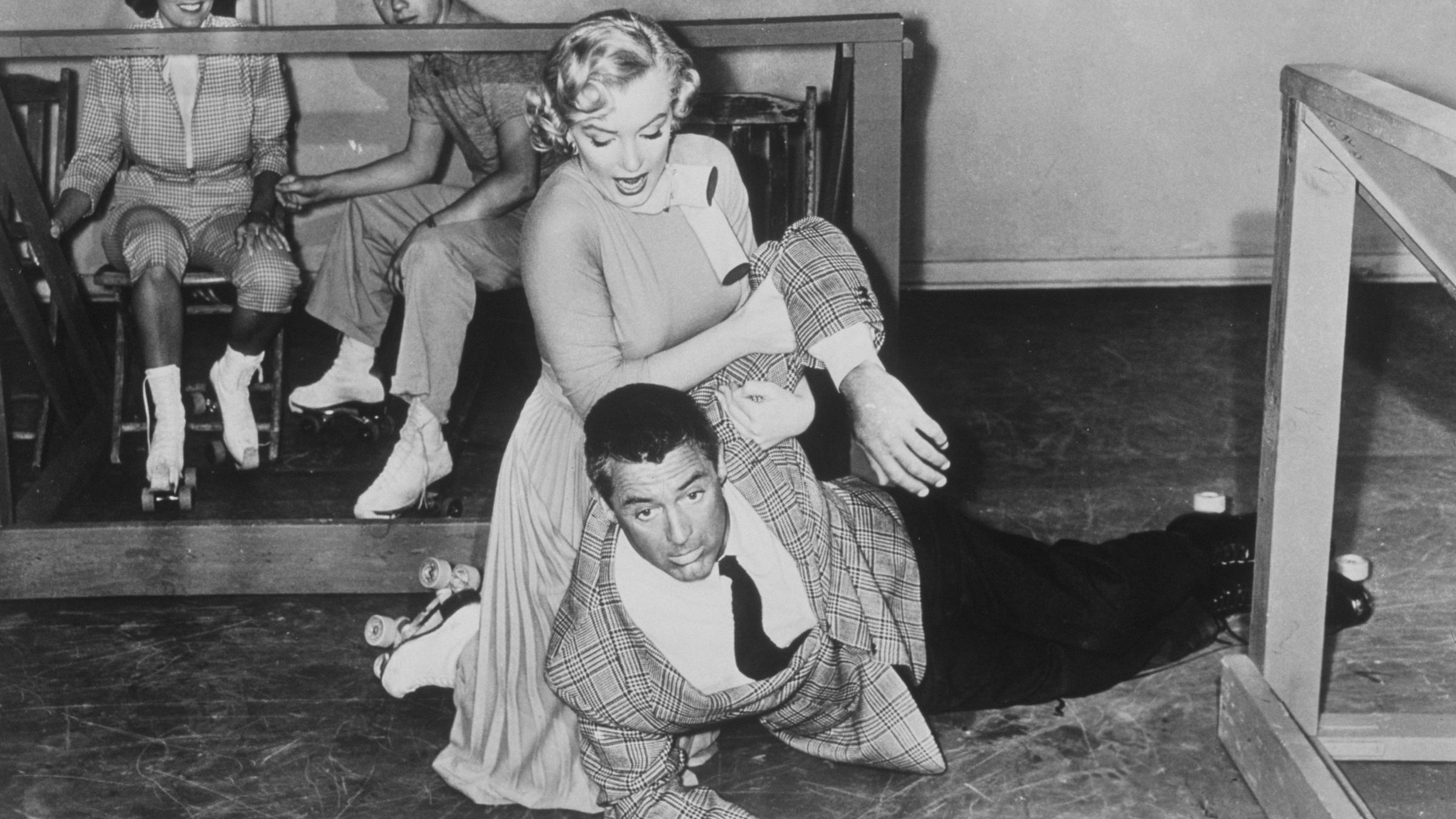"Liebling, ich werde jünger": Der Wissenschaftler Barnaby Fulton (Cary Grant) ist mit der Sekretärin seines Chefs Lois Laurel (Marilyn Monroe) auf der Rollschuhbahn. Barnaby, der ein auffälliges großkariertes Sakko und einen jugendlichen Kurzhaarschnitt trägt, liegt der Länge nach auf dem Boden und schaut erschreckt. Lois kniet im hellen Kleid mit weißem Schal hinter ihm und versucht, ihm aufzuhelfen.