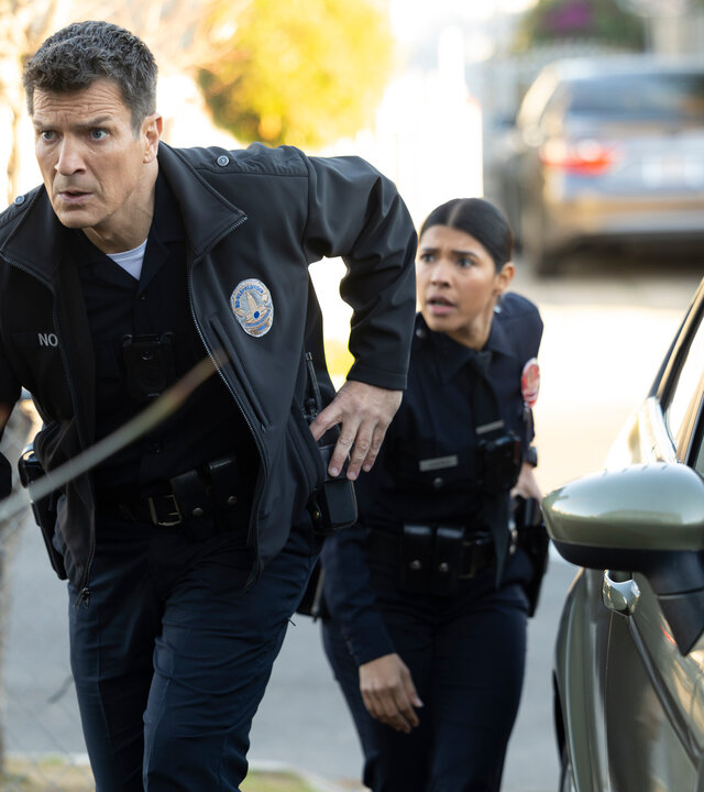 "The Rookie - Geheimnisse und Lügen": Officer Juarez (Lisseth Chavez) und Nolan (Nathan Fillion) schleichen sich auf ein Privatgrundstück und blicken konzentriert in dieselbe Richtung, während jeder von ihnen seine Hand an der Dienstwaffe hat.