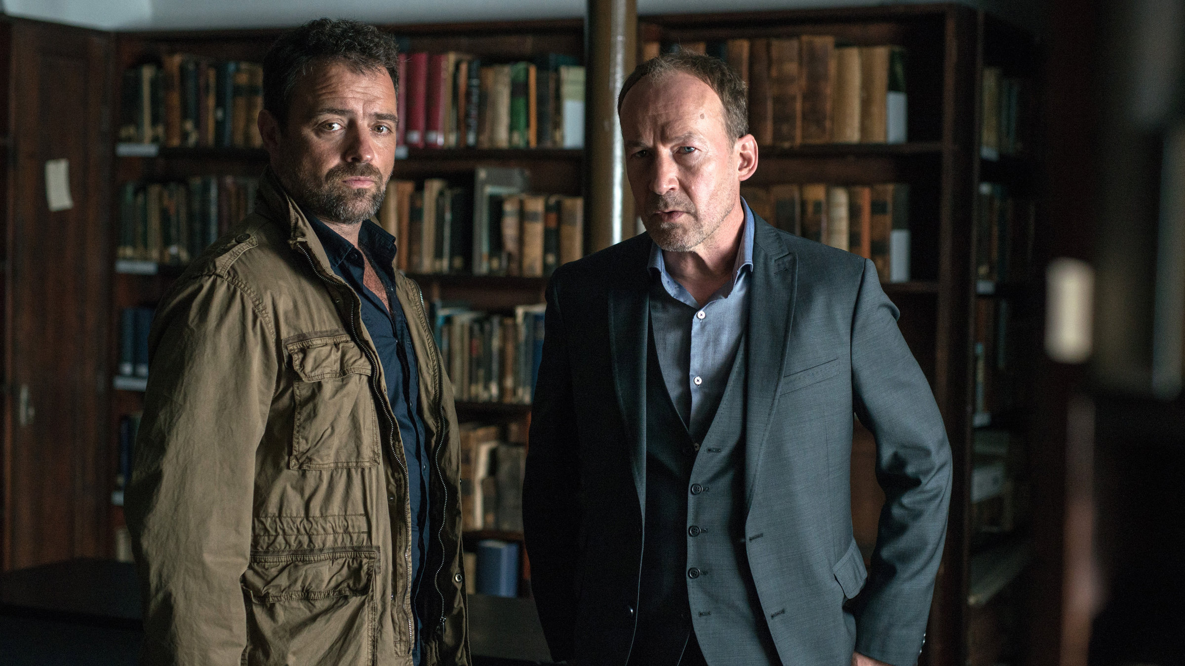 "Neben der Spur - Todeswunsch": Joe (Ulrich Noethen) und Vincent (Juergen Maurer) stehen in einer Bibliothek und suchen etwas.