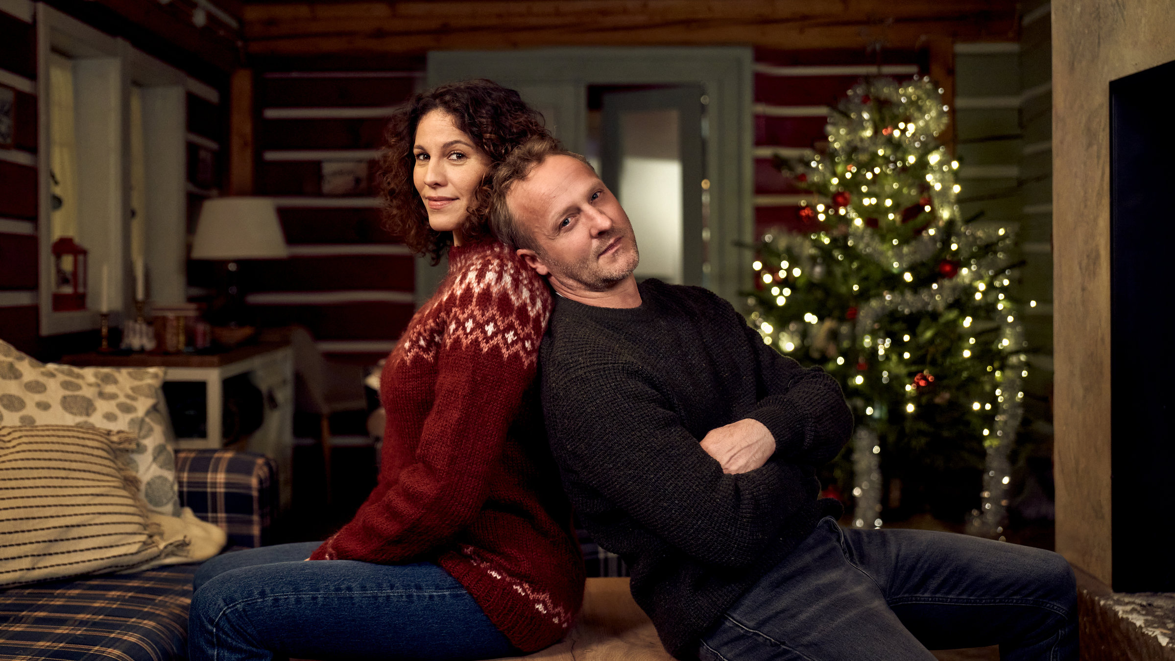 "Ein Regenbogen zu Weihnachten": In einer  gemütlich eingerichteten Skihütte sitzen Nicole Golding (Jasmin Gerat) und Martin Kupfer (Maximilian Brückner) Rücken an Rücken und schauen lächelnd in die Kamera. Im Hintergrund steht ein festlich geschmückter Weihnachtsbaum.