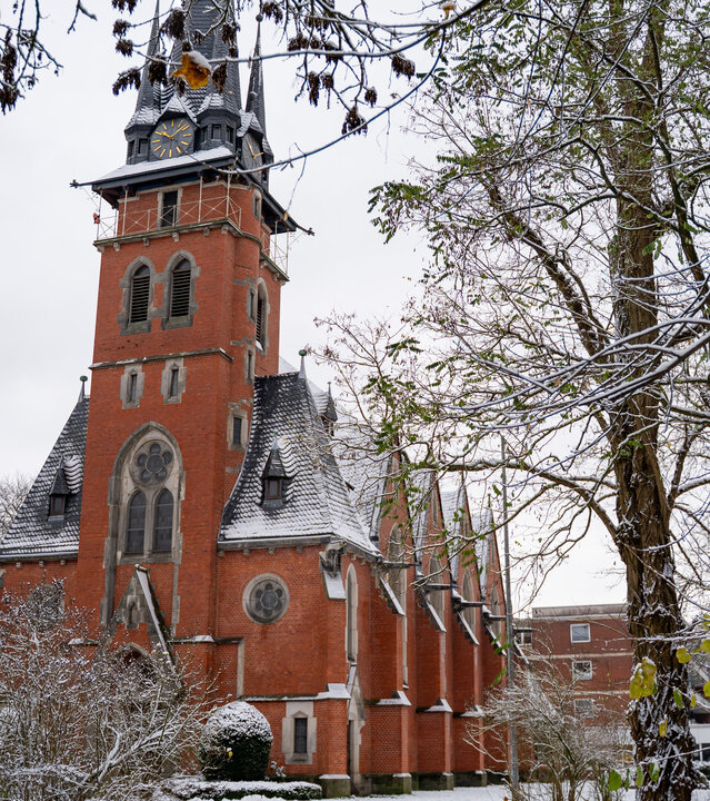 "Evangelischer Gottesdienst - Ihr sollt sicher wohnen: Housing first": Das Bild zeigt die filigran gebaute Stiftskirche des Stephanstifts in Hannover. Die Kirche ist aus roten Steinen erbaut, umgeben von verschneiten Bäumen.