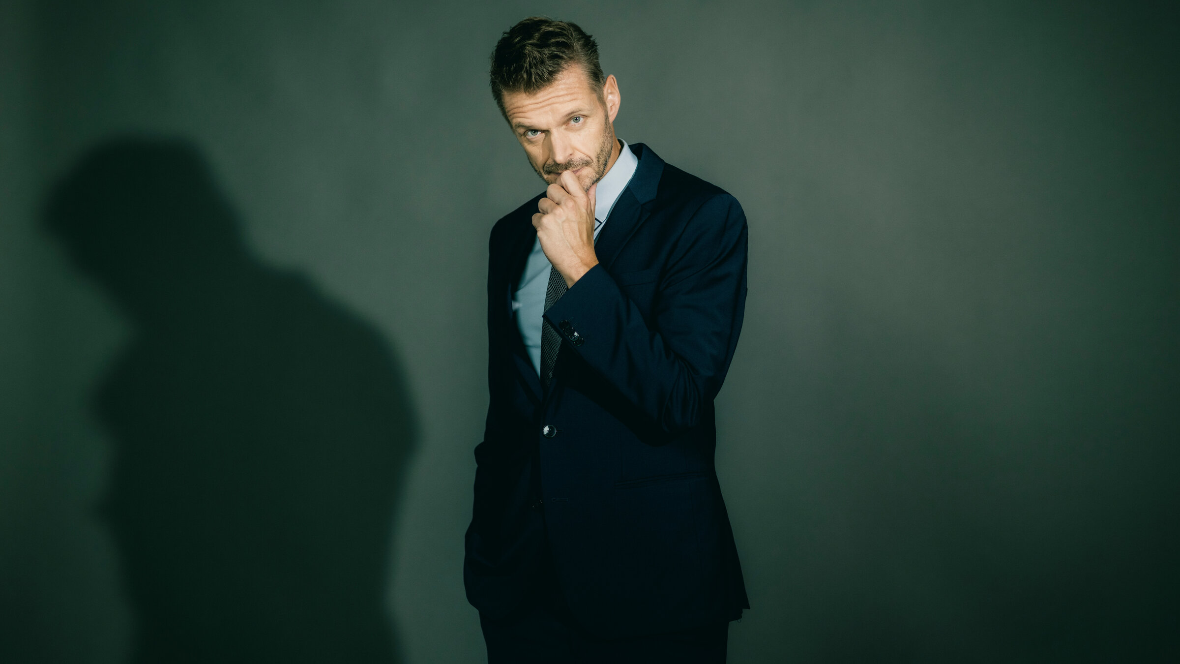 "JOURNAL DELUXE": Florian Schroeder steht in der Mitte des Bildes. Er trÃ¤gt einen dunklen Anzug. Auf der linken Seite ist sein Schatten zu sehen. Er hÃ¤lt seine rechte Hand vor sein Kinn.