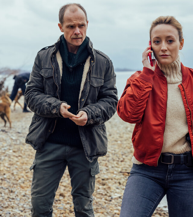"Die Toten vom Bodensee - Die Medusa": Micha Oberländer (Matthias Koeberlin) und Luisa Hoffmann (Alina Fritsch) stehen zusammen am Ufer. Luisa Hoffmann (Alina Fritsch) telefoniert mit dem Handy.