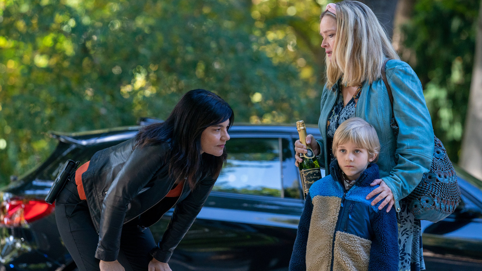 "Letzte Spur Berlin - Der Wanderer": Mina Amiri (Jasmin Tabatabai) beugt sich zu Ben Brackert (Florian Simon), der zusammen mit seiner Oma Elena Brackert (Julia Biedermann) vor einem Auto stehen.