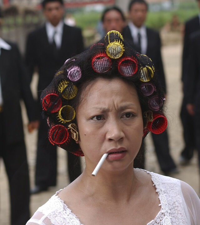 "Kung Fu Hustle": Auf einem Dorfplatz steht die Landlady (Qiu Yuen) im Nachthemd, mit Lockenwicklern im Haar und einer Zigarette im Mund. Hinter ihr haben sich die Männer der Axt-Gang versammelt.