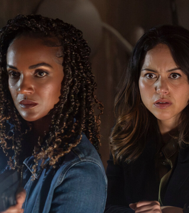 "The Rookie - Dunkelheit": Detective Nyla Harper (Mekia Cox) und Officer Angela Lopez (Alyssa Diaz) stehen nebeneinander in einem verlassenen Raum. Beide tragen Alltagskleidung und halten leuchtende Taschenlampen in der Hand. Harper führt noch zusätzlich eine Waffe in der anderen Hand. Beide blicken in dieselbe Richtung, während neben ihnen ein zerrissener Plastikvorhang hängt.