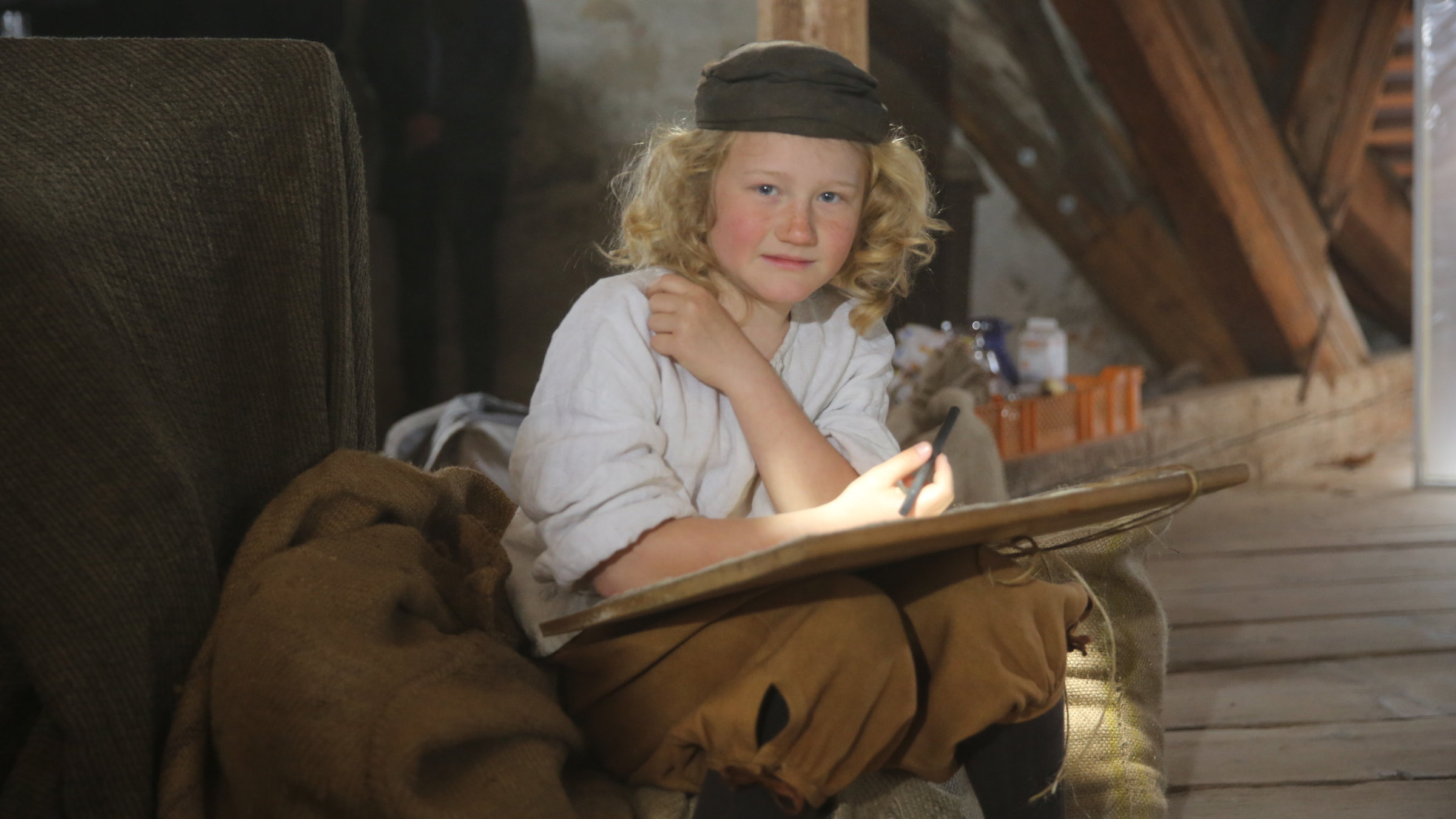 "Terra X: Giganten der Kunst - Rembrandt": Spielszene: Rembrandt als Kind (Anthony Schaefer) sitzt auf einem Sack und hat eine Malvorlage auf den Knien.