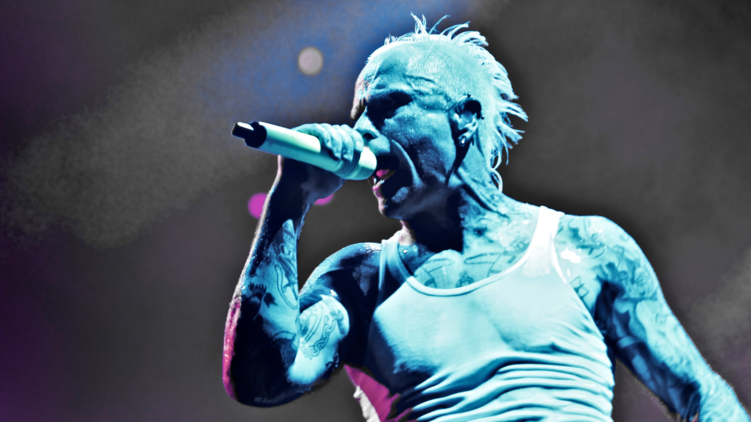"Pop Around the Clock – Summer Edition: The Prodigy: World´s on Fire": Ein verschwitzter Mann mit weißem Unterhemd und vielen Tattoos hält sich ein Mikrofon vor den Mund während er singt. er wird von bläulichem Licht angestrahlt.