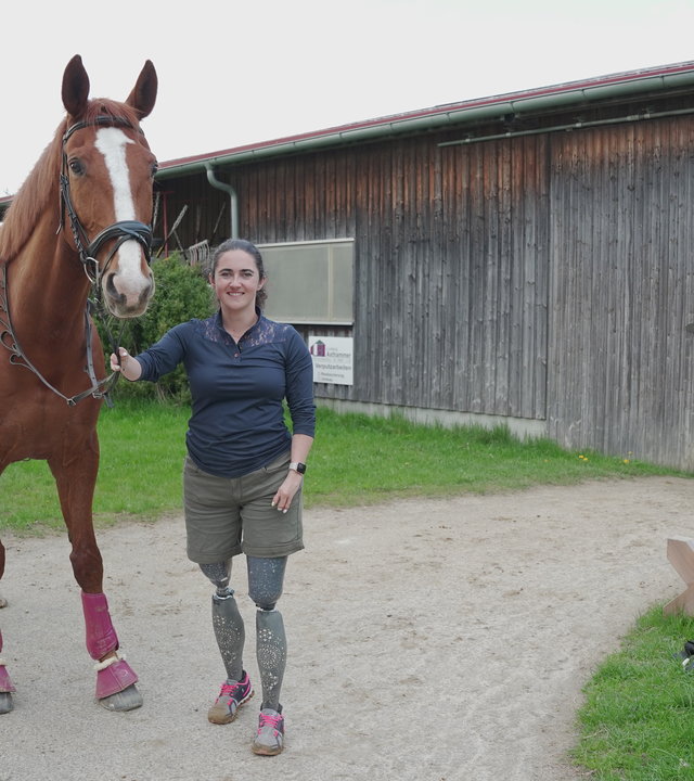 "einfach Mensch - Julia Porzelt: Nicht ohne mein Pferd!": Julia Porzelt steht mit ihrem Pferd Bruno vor einer Reithalle.