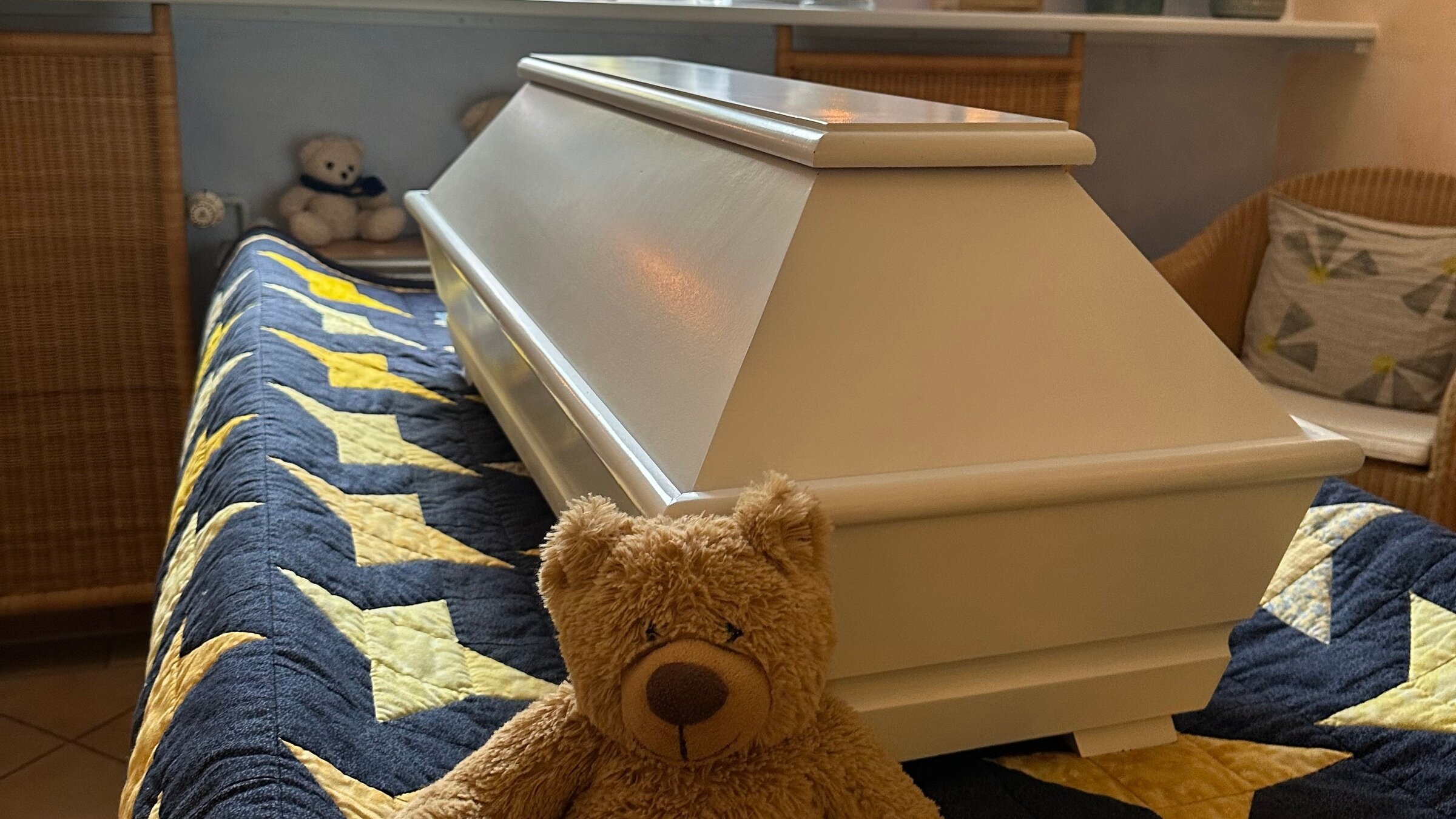 "Tabu Tod (1/2) - Sterben heute": Heller Kindersarg auf einer Sternendecke, davor ein Teddy, im Hintergrund ein Buntglasfenster und brennende Windlichter.