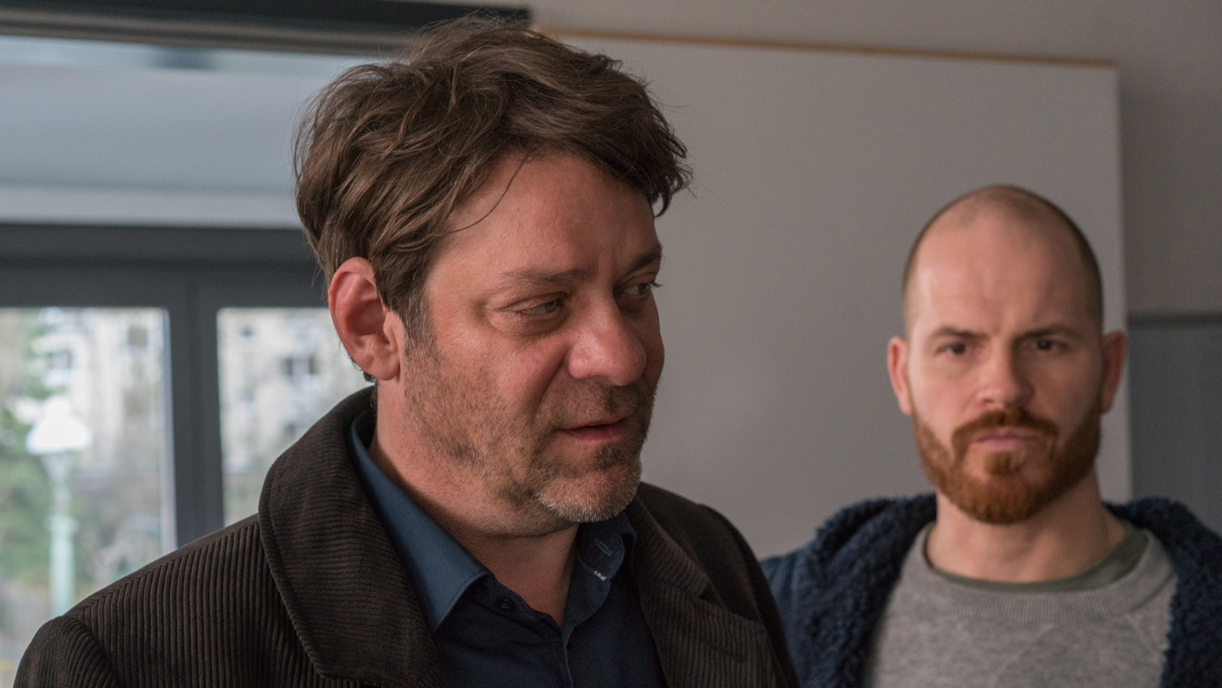 "Der Kommissar und die Wut": Martin Brühl (Roeland Wiesnekker) schaut zur Seite. Hinter ihm steht Eli Wiesner (Marc Ben Puch).