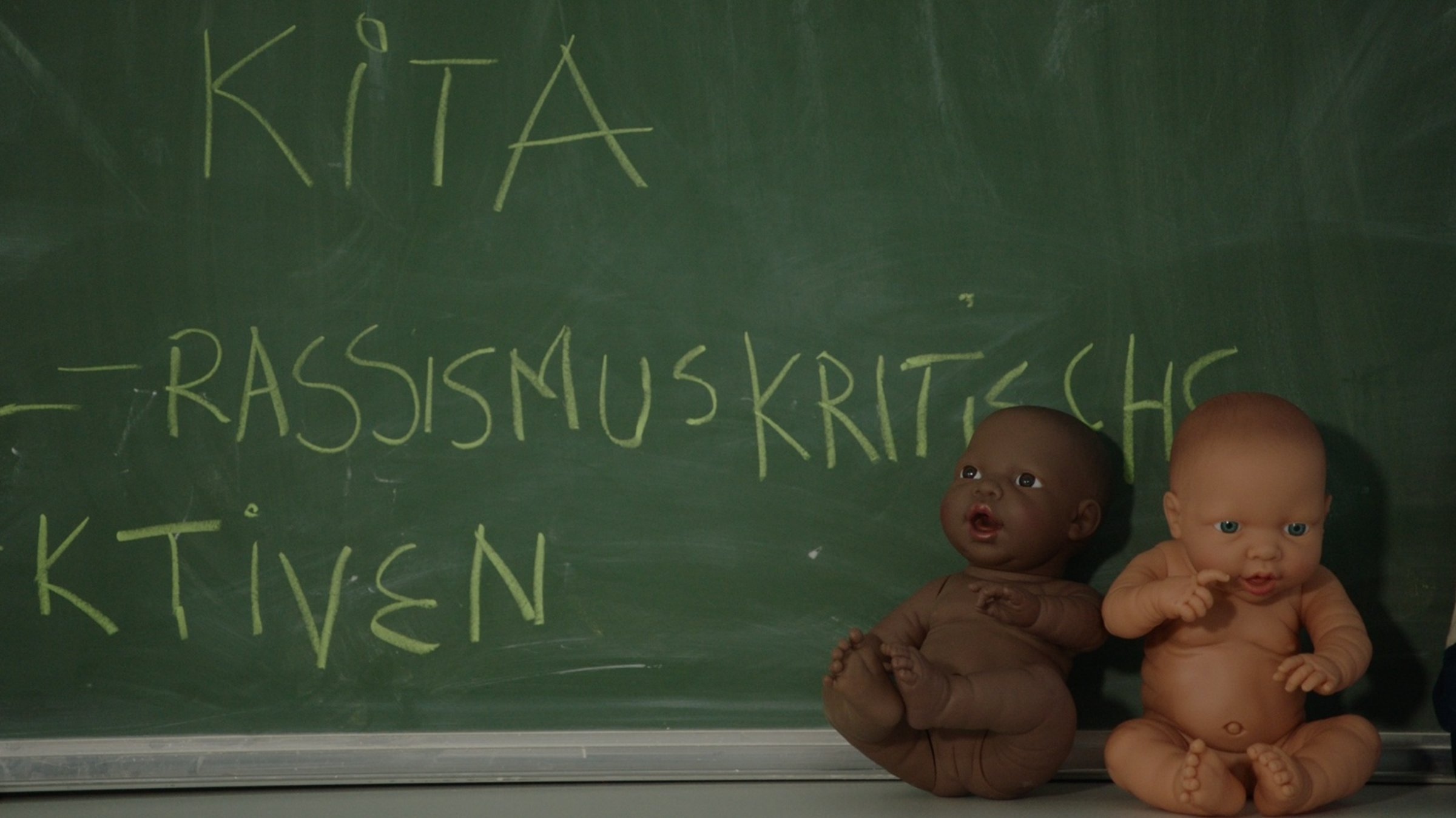 Die Macht der Vorurteile - Rassismus bewusst verlernen!: Zwei Puppen mit unterschiedlicher Hautfarbe sitzen vor einer Schultafel.