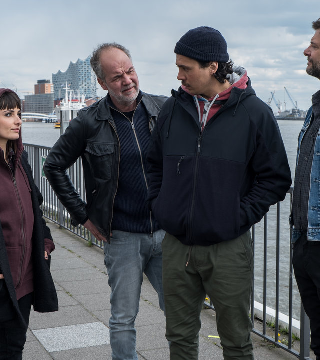 "SOKO Hamburg - Schlangengrube": Franzi Berger (Paula Schramm) und Oskar Schütz (Marek Erhardt) stehen mit Amar Rajap (Rahul Chakraborty) vor einem Geländer am Hafen. Oskar Schütz steht hinter Amar Rajap und sieht diesen skeptisch an. Amar blickt unsicher zurück und hat die Hände in den Jackentaschen vergraben. Rechts neben ihm steht Jörg Hammerschmidt (Mike Olsowski), der ebenfalls zu Oskar Schütz blickt.