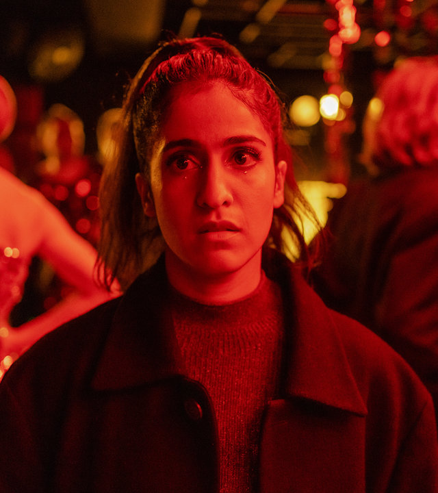 "Loving Her - Loving Truth": Großaufnahme von Hanna (Banafshe Hourmazdi). Sie steht in einem Club. Hinter ihr stehen Menschen (Komparsen), die sich miteinander unterhalten. Sie schaut nachdenklich ins Leere.