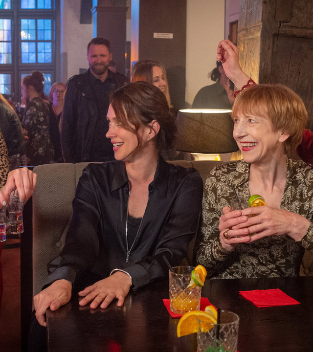 „SOKO Wismar – Girls‘ Night“: Stine (Sidsel Hindhede), Karoline (Nike Fuhrmann), Helene (Katharina Blaschke) und Roswitha (Silke Matthias) haben sich schick gemacht. Während Karoline, Helene und Roswitha nebeneinander an einem Tisch sitzen, bringt Stine vier Schnapsgläser von der Bar. Alle vier strahlen einander an, es herrscht eine ausgelassene Stimmung. Im Hintergrund stehen Menschen an der Bar.