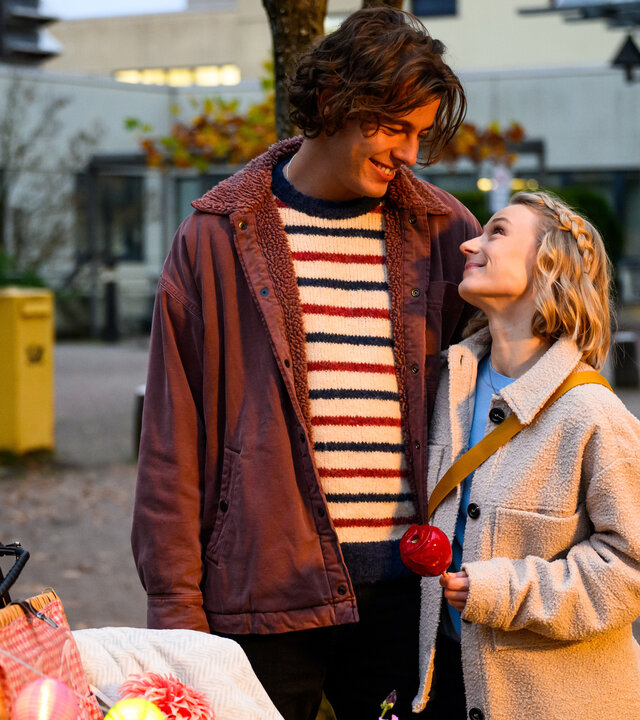 "Bettys Diagnose - Spielereien": Auf einem kleinen Platz in der Stadt: Simon (Ivan Barišić) hält Mia (Antonia Döring) im Arm und schaut sie verliebt an. Im Vordergrund steht ein Lastenfahrrad mit einer Lichtergirlande, am Lenker hängt ein Fahrradhelm. Im Hintergrund steht ein großer, gelber Briefkasten.