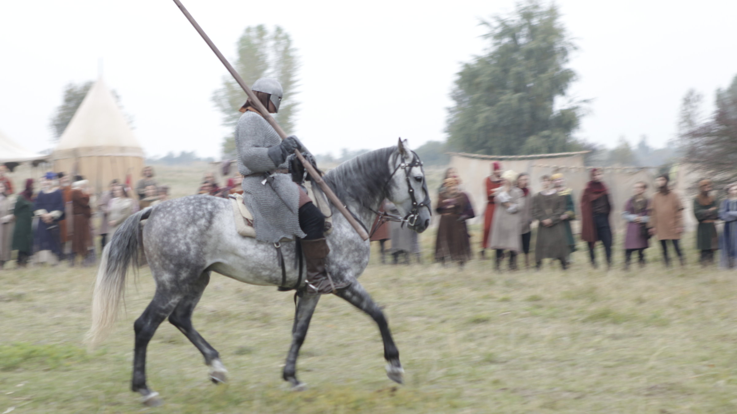 "Terra X: Die Welt der Ritter - 1. Männer in Eisen": Spielszene: Ein Ritter auf seinem Pferd trägt eine Lanze in der rechten Hand. Im Hintergrund ist Publikum zu sehen.