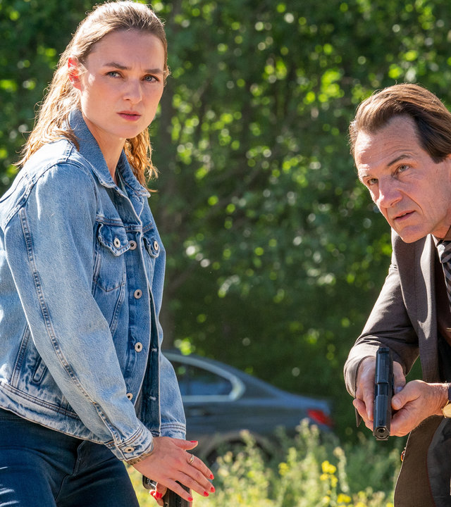 "Letzte Spur Berlin - Volles Risiko": Lucy Elbe (Josephin Busch) und Oliver Radek (Hans-Werner Meyer) stehen mit ihren Waffen einsatzbereit hinter einem Auto auf einer Wiese.