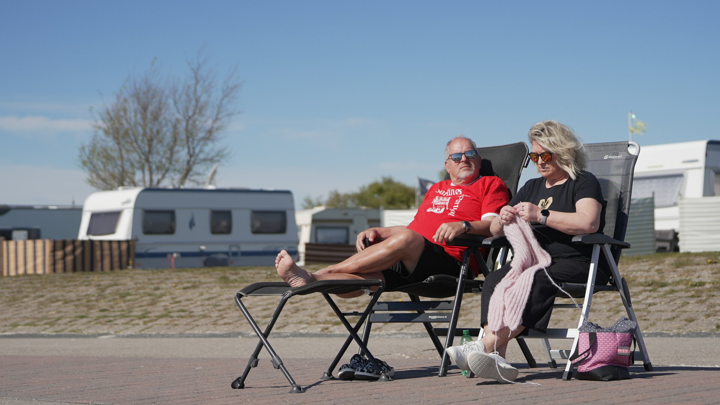 "ZDF.reportage: Leben auf dem Campingplatz - Zwischen Räumung und Neuanfang": Kristina Schumann und ihr Mann Manfred sitzen auf Campingstühlen vor ihrem Wohnwagen und genießen die Sonnenstrahlen.