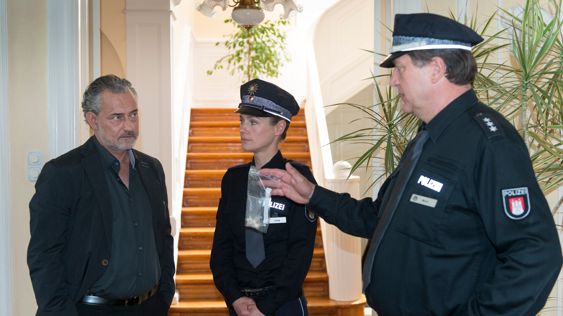 "Notruf Hafenkante: In der Falle": Franzi (Rhea Harder) und Hans (Bruno F. Apitz) stehen in einem Hausflur Lars Paulsen (Rolf Kanies) gegenüber und sehen ihn eindringlich an.