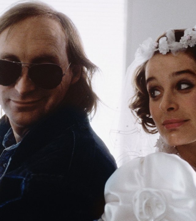 "Otto - Der Liebesfilm": Otto (Otto Waalkes) und Tina (Jessika Cardinahl) sitzen Rücken an Rücken zueinander. Otto hat eine schwarze Lederjacke und Sonnenbrille an, während Tina ein Brautkleid trägt.
