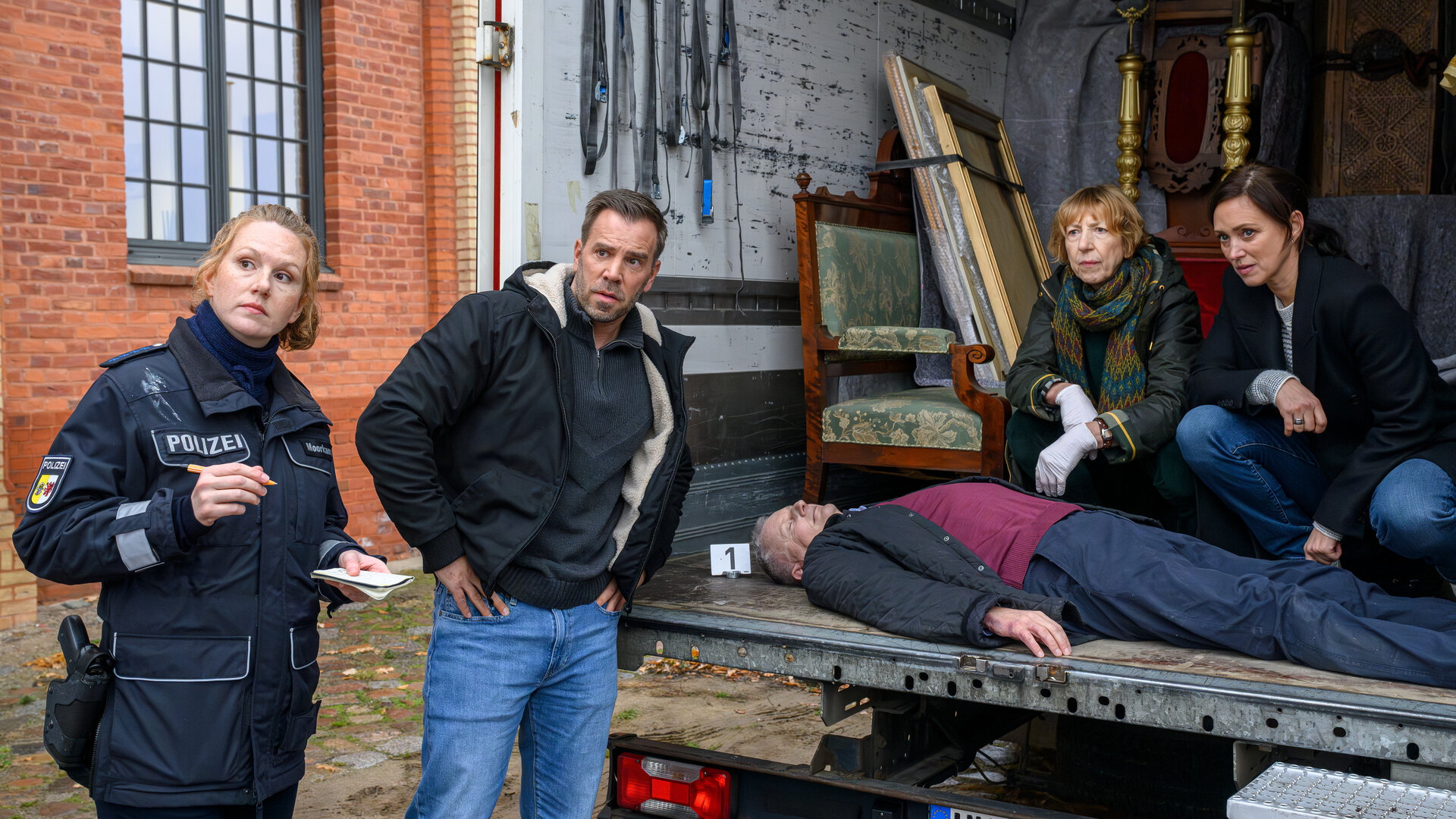 "SOKO Wismar â Der letzte Umzug": Auf der LadeflÃ¤che eines Umzugswagens untersuchen Dr. Helene Sturbeck (Katharina Blaschke) und Karoline Joost (Nike Fuhrmann) die Leiche von Werner Tessmer (Komparse). Vor dem geÃ¶ffneten Lkw stehen Paula Moorkamp (Stella Hinrichs) und Lars PÃ¶hlmann (Dominic Boeer). Alle schauen gespannt seitlich nach vorne.