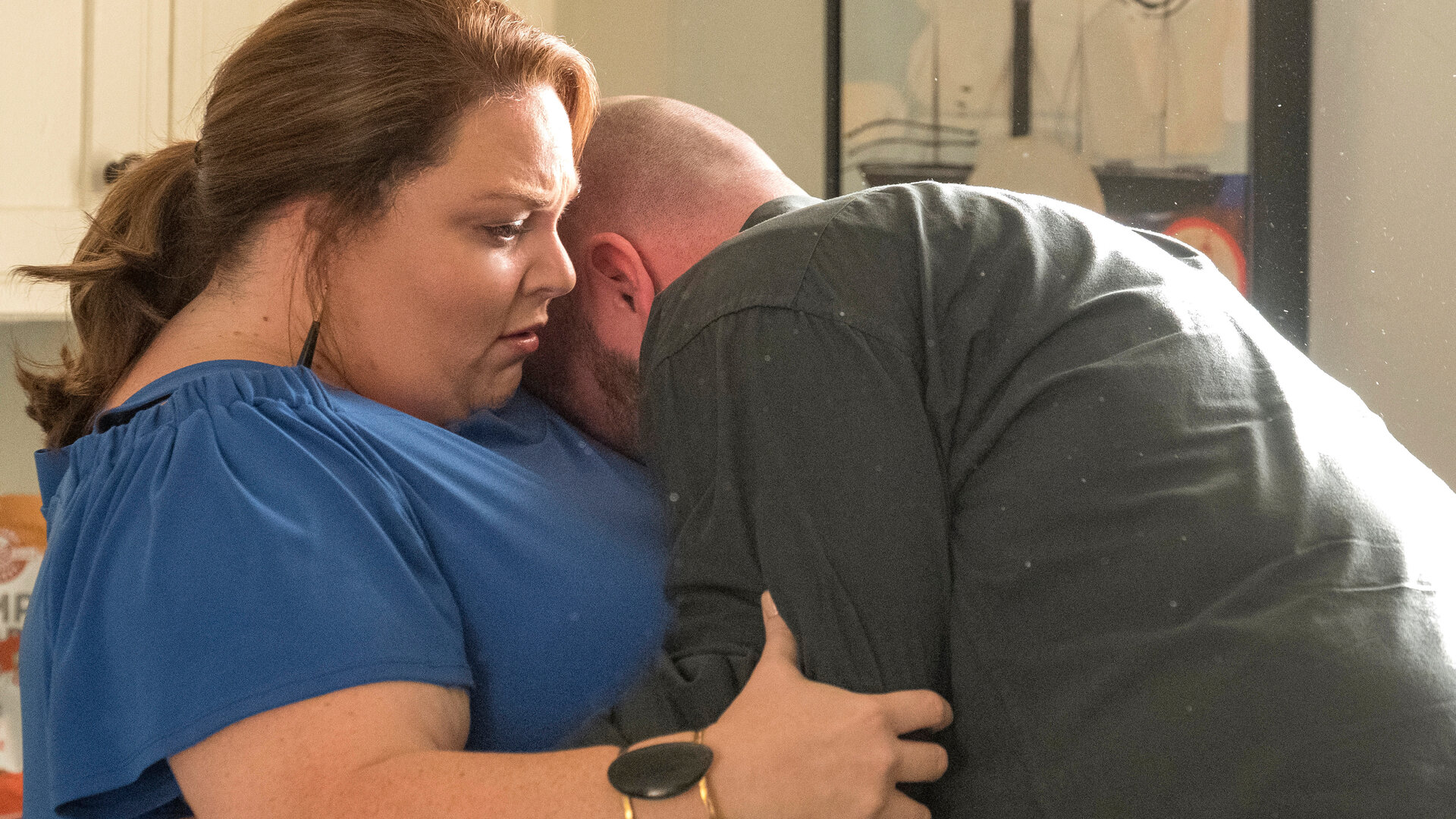 "This Is Us - Toby": Kate (Chrissy Metz) und Toby (Chris Sullivan) stehen in der Küche. Kate blickt verwundert nach vorn und umarmt Toby. Toby vergräbt sein Gesicht in Kates Schulter und erwidert die Umarmung.