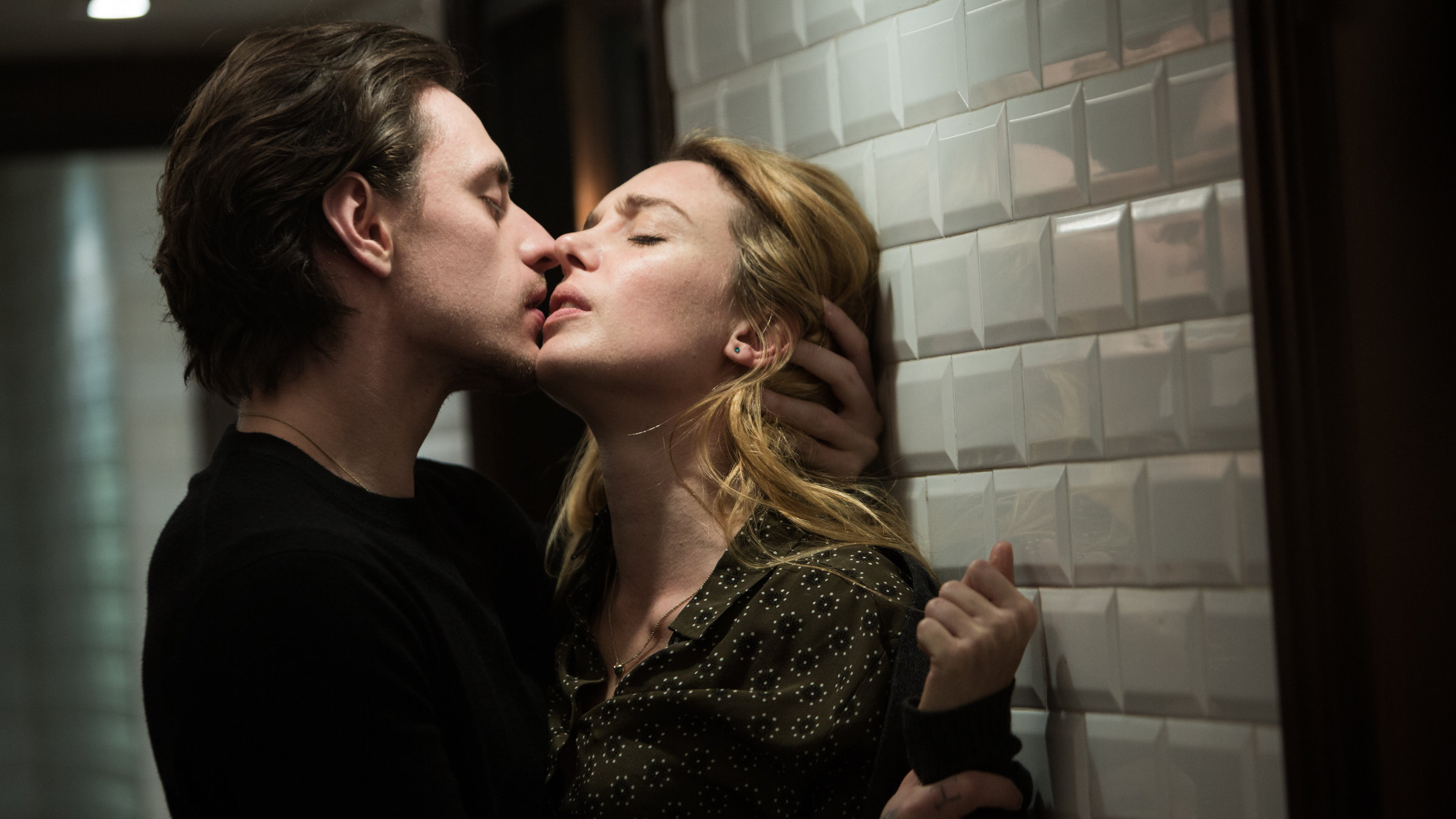 „Passion Simple“: Hélène (Lætitia Dosch) befindet sich mit dem Rücken zu einer Wand, die von oben beleuchtet ist. Alexandre (Sergej Polunin) steht ihr gegenüber und hält sie am linken Handgelenk fest, kurz bevor er sie küsst.