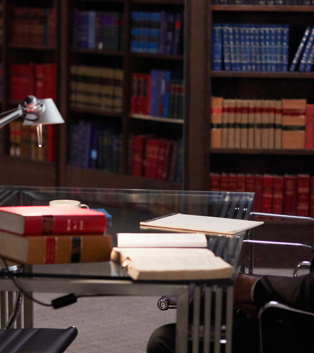 "Suits - Verletzter Stolz": Harvey (Gabriel Macht) und Samantha (Katherine Heigl) sitzen sich an einem Glastisch gegenüber. Sie schauen sich erwartungsvoll an. Im Hintergrund sind gefüllte Bücherregale zu erkennen.