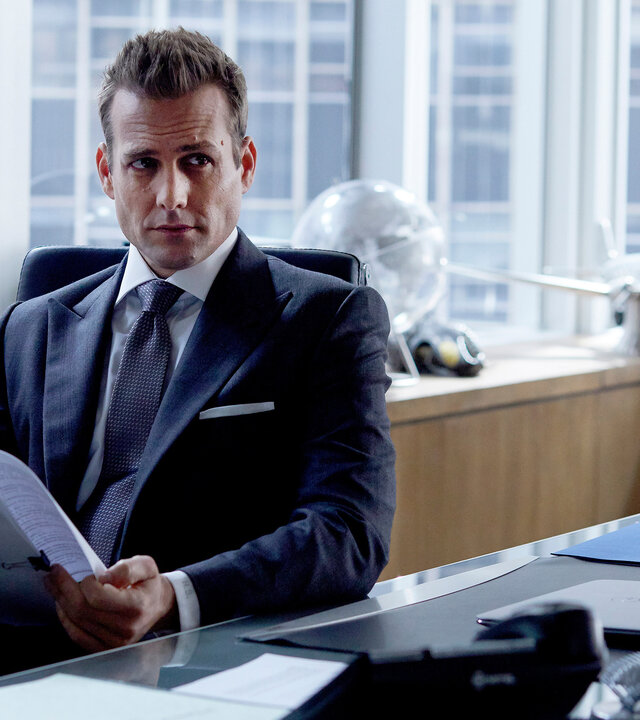 "Suits - Lampenfieber": Harvey sitzt am Schreibtisch und hält eine Akte in den Händen. Abgelenkt schaut er erwartungsvoll auf. Im Hintergrund sind durch die Fensterfront Hochhäuser New Yorks zu erkennen.