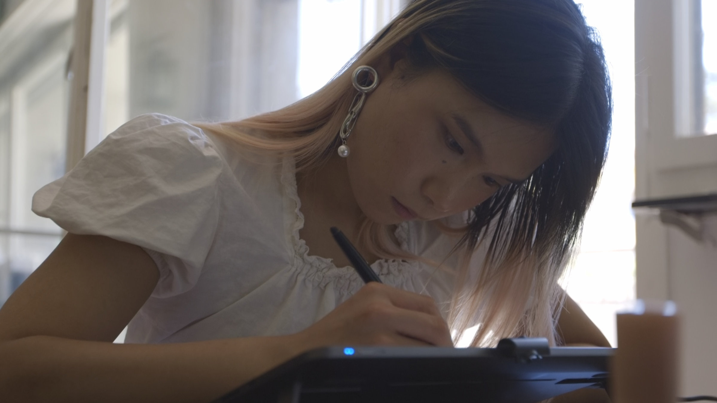 "Ab 18! - Chao's Transition": Nahaufnahme einer jungen Frau, die sich mit einem Stift in der Hand über ein Grafiktablett beugt.