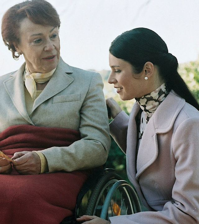 "Bianca - Wege zum Glück: Folge 49": Spaziergang im Park: Judith (Elisabeth Suttrlüty) kniet neben Oma Ursula (Annemone Haas), die im Rollstuhl sitzt und freundlich zu Judith schaut.