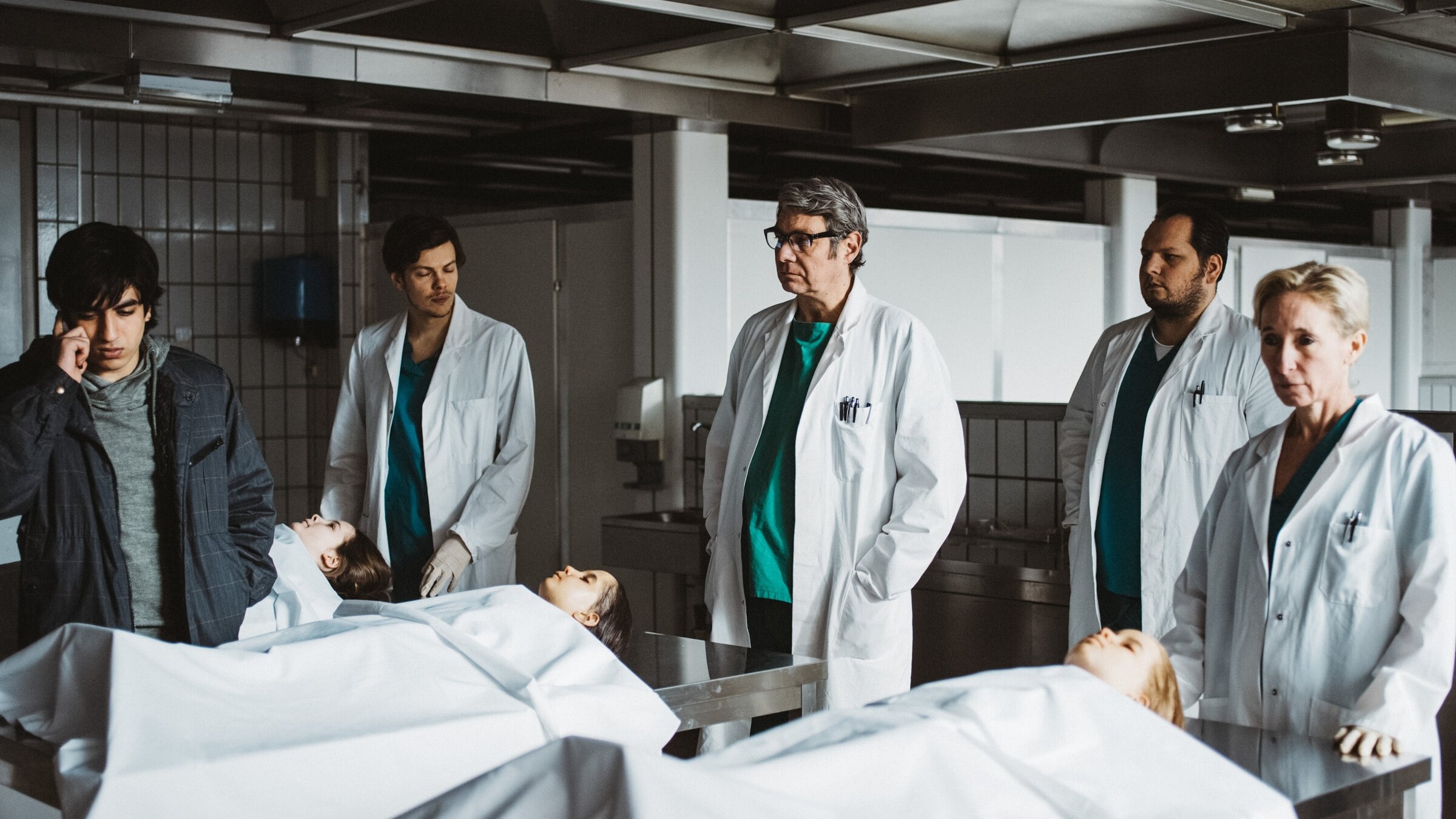 "M - Eine Stadt sucht einen Mörder (3/6)": Omid Memar (Junger Afghane, li.), Hakon Hirzenberger (Pathologe, 3.v.li.).